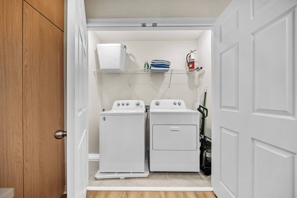 This practical laundry area features a pair of sleek white appliances, neatly arranged within a bright, clean space. The light wood flooring adds warmth, while the organized layout ensures convenience during your stay.