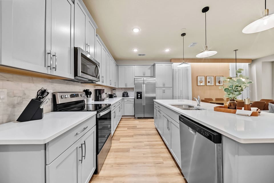 Discover a culinary haven in this inviting kitchen with sleek white cabinetry, a spacious island for gatherings, warm wood flooring, and modern stainless steel appliances, all lit by soft pendant lights for a stylish atmosphere.