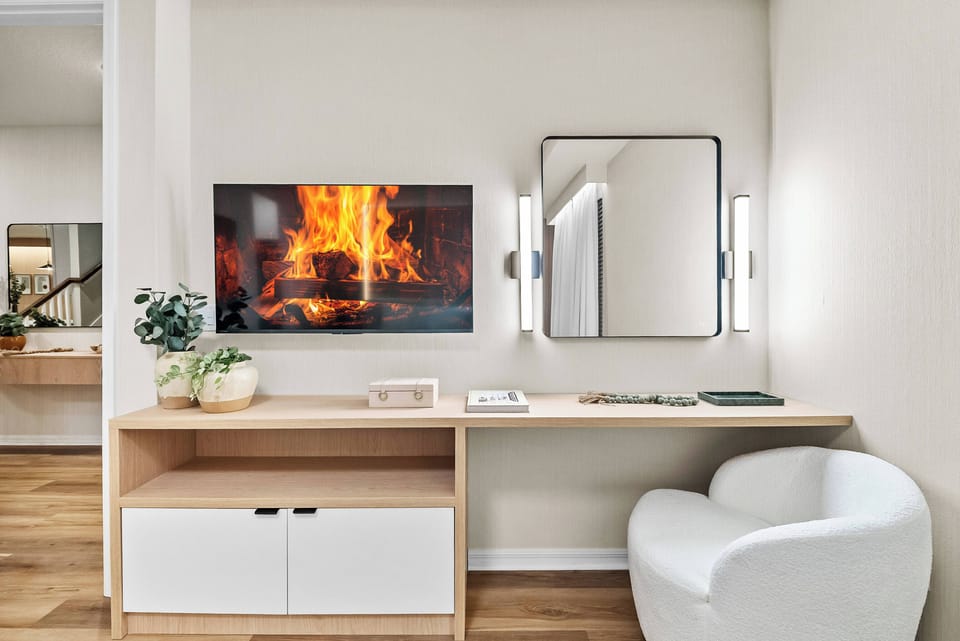 This cozy nook offers a sleek wooden console and a soft white chair, creating a stylish spot to unwind. Enjoy the wall-mounted TV, modern lighting, and mirror that together create a warm atmosphere with a flickering fire display.