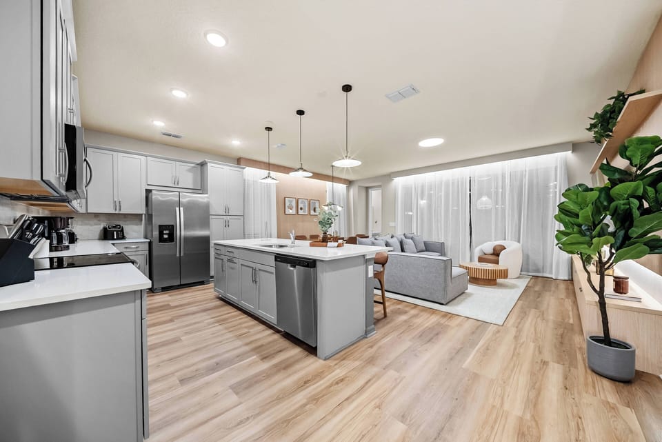 Experience the heart of your vacation in this beautifully designed kitchen and living area, featuring sleek gray cabinets, a spacious meal prep island, warm wood floors, and abundant natural light for a welcoming atmosphere.
