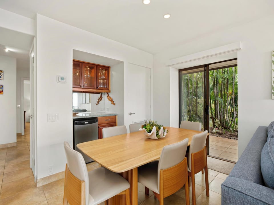 Gather around the warm wood dining table and enjoy meals together in this bright, open space. Natural light pours in through the patio door, framing lush greenery and creating a peaceful atmosphere for your morning coffee or evening dinner.