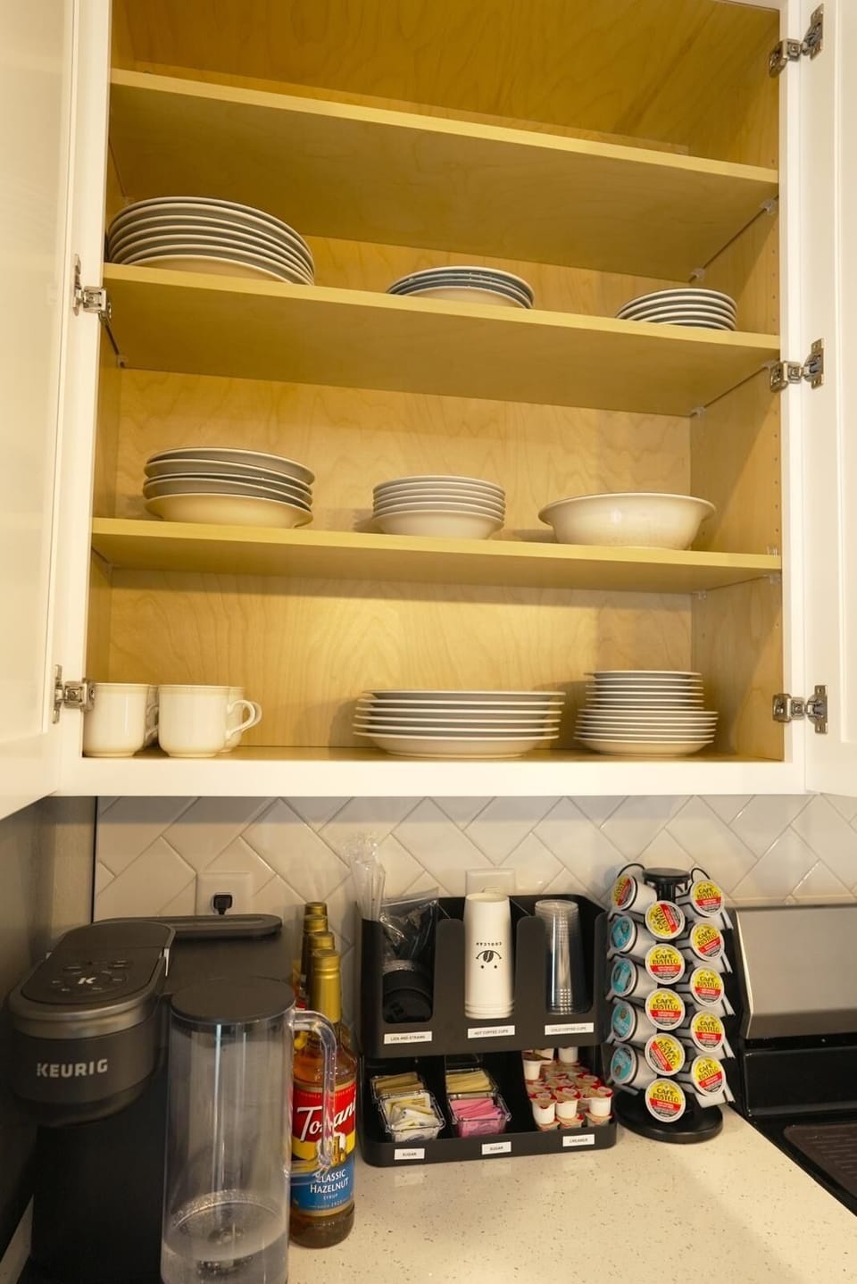 Well-equipped kitchen cabinet with dishes and Keurig coffee setup.