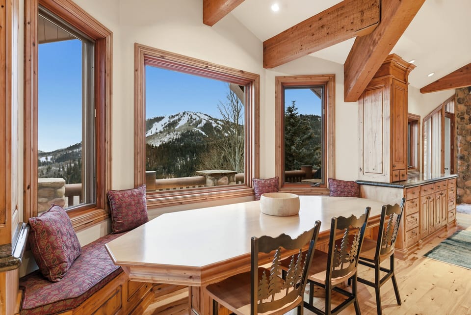 Breakfast nook with panoramic windows:
Bright breakfast nook with built-in seating, wood table, and expansive windows overlooking snow-covered mountain scenery.