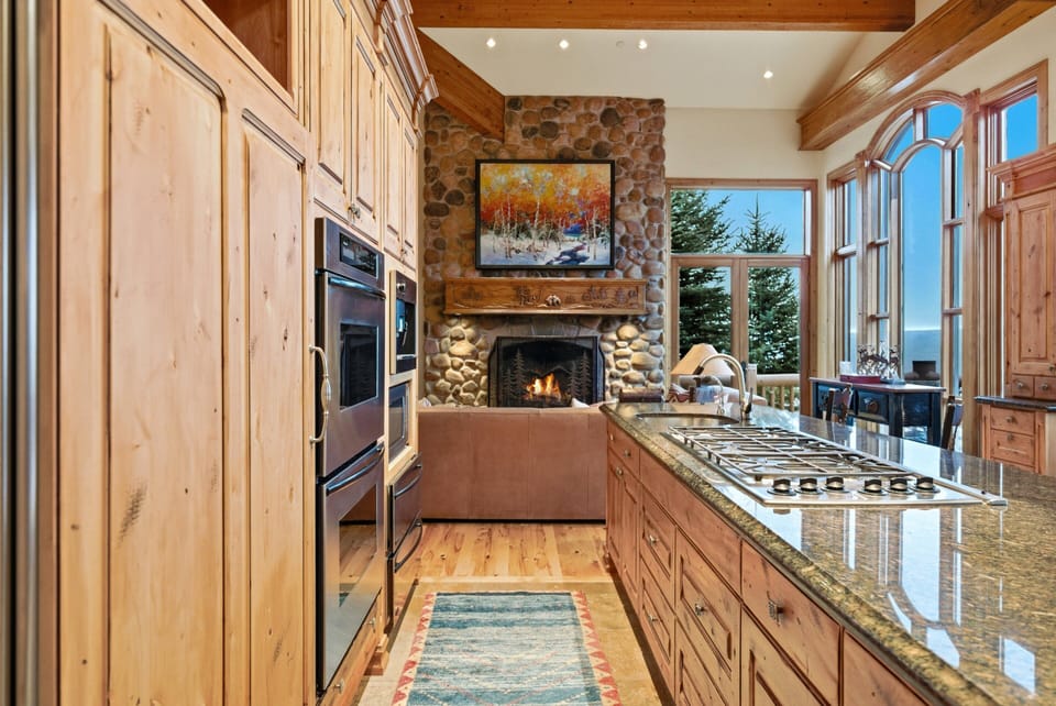 Kitchen island and living area:
Luxury kitchen island with granite countertops, wood cabinetry, and a view into the living area with stone fireplace.