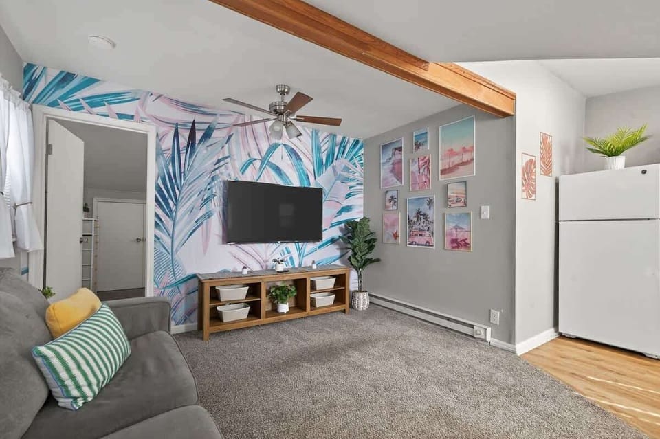 Another view of the living room highlights playful tropical accents and comfortable seating. The TV wall creates a perfect spot for relaxing movie nights. 