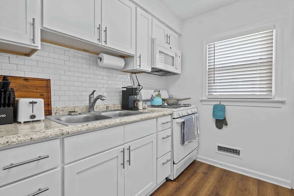Cook in a clean, modern kitchen w/ sleek counters, white cabinetry & natural light