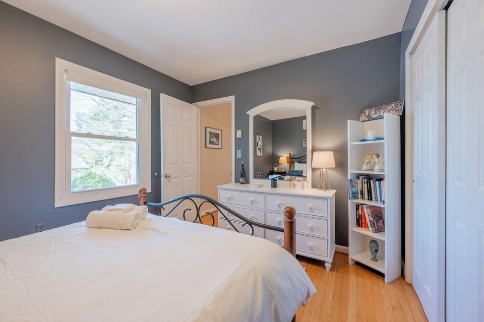 Bright, serene bedroom with soft gray walls, hardwood floors, and a classic white dresser and mirror