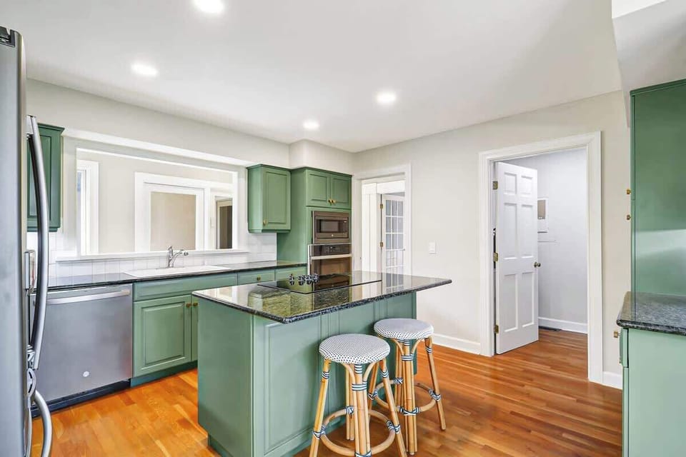 The fully-equipped kitchen features sage green cabinets, granite countertops, and a breakfast bar perfect for morning coffee or casual meals.