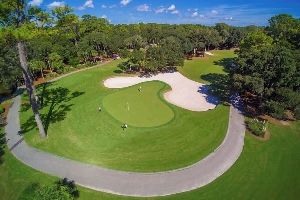 Aerial view of pristine golf course with sand bunkers and lush green fairways surrounded by mature trees.
