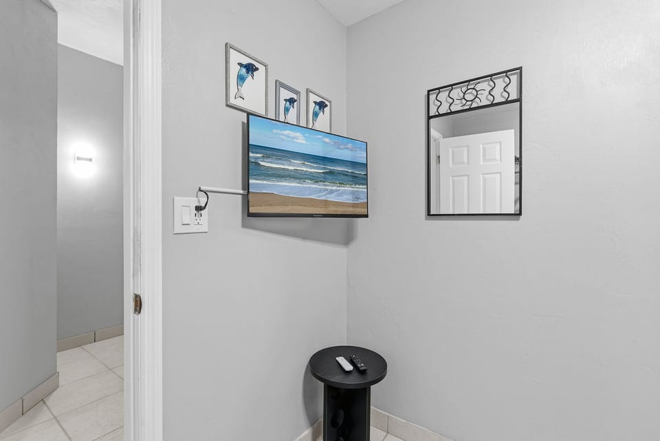 Enjoy this cozy beach stay nook featuring a wall-mounted TV and mirror—perfect for relaxing, catching your favorite shows, or unwinding after a day at the beach.