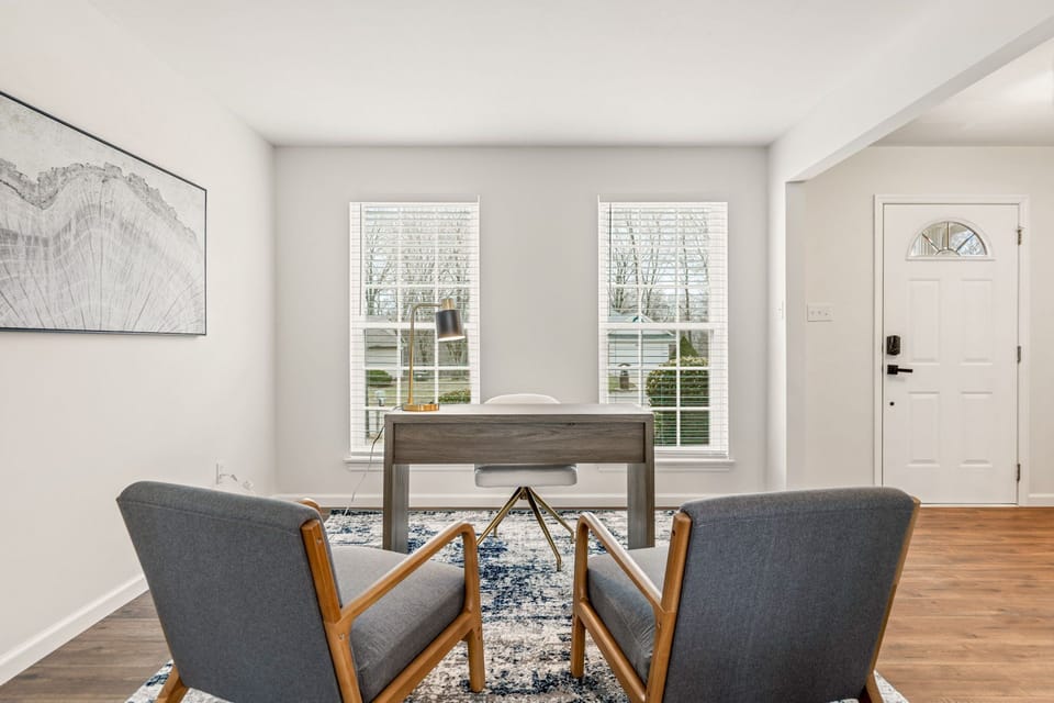 A reverse office view shows two upholstered chairs facing a desk positioned between tall windows.