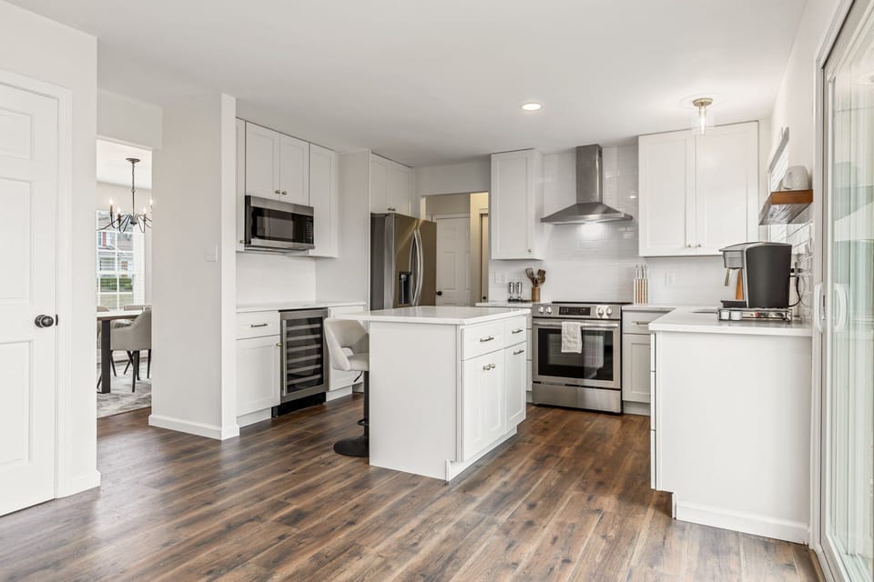The open kitchen features white cabinetry, generous counters, and stainless-steel appliances beside the living area.