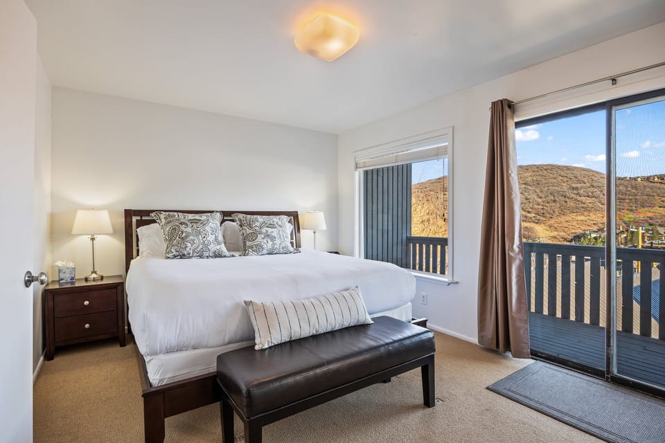 Bright and comfortable master bedroom featuring a king bed and private balcony access, offering peaceful mountain views and plenty of natural light.