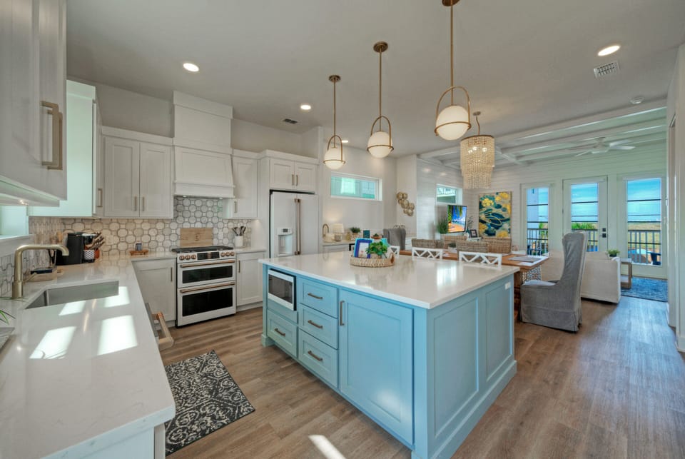 Open-concept kitchen with light blue island, white cabinetry, and hanging pendant lights.