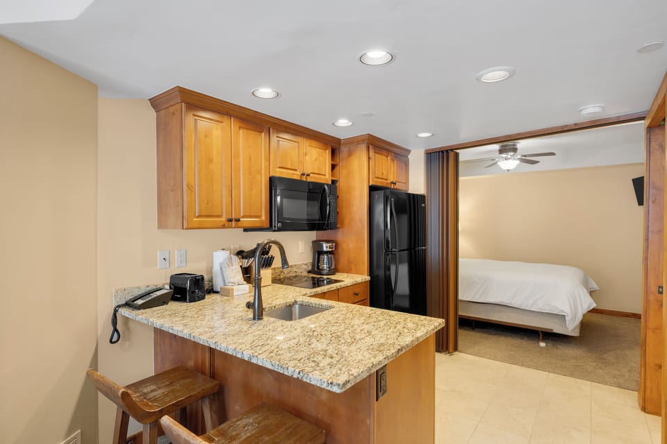 Your open-concept suite features a kitchenette with granite countertops and modern appliances, seamlessly flowing into your comfortable bedroom space.