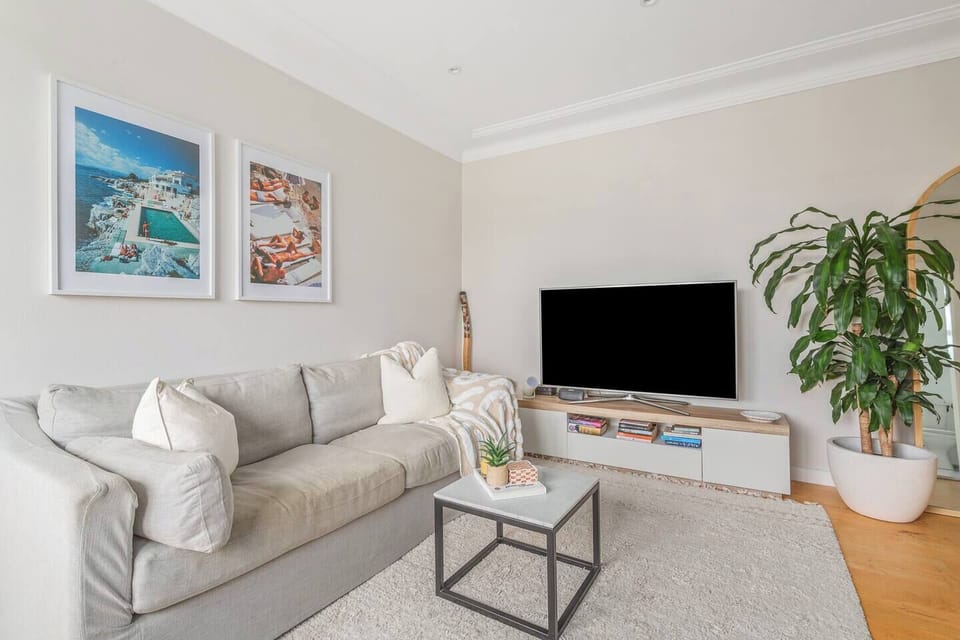 The sunlit living area invites slow mornings and unwinding evenings, featuring a plush sofa, curated artwork, a TV and leafy outlooks that connect the space to the outdoors.