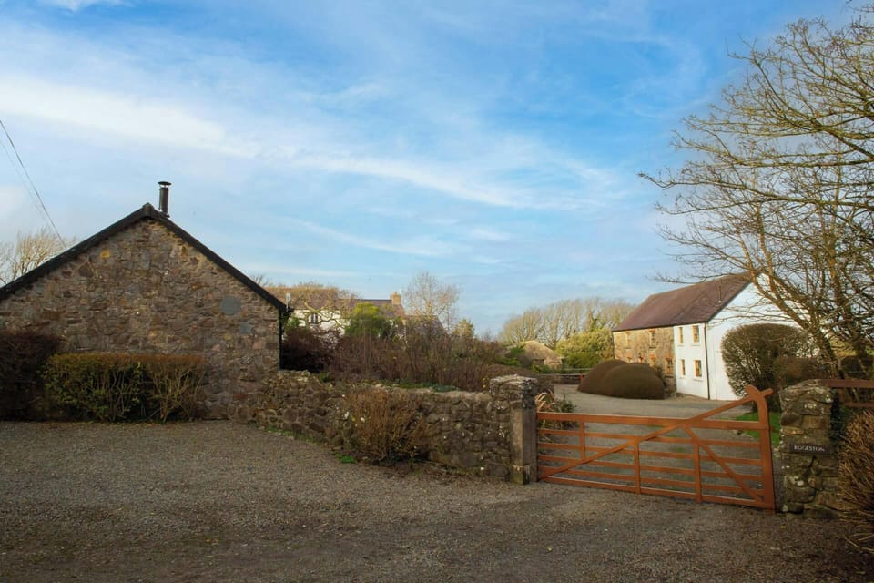 Gravel yard with stone walls, wooden gate and two houses under a blue sky