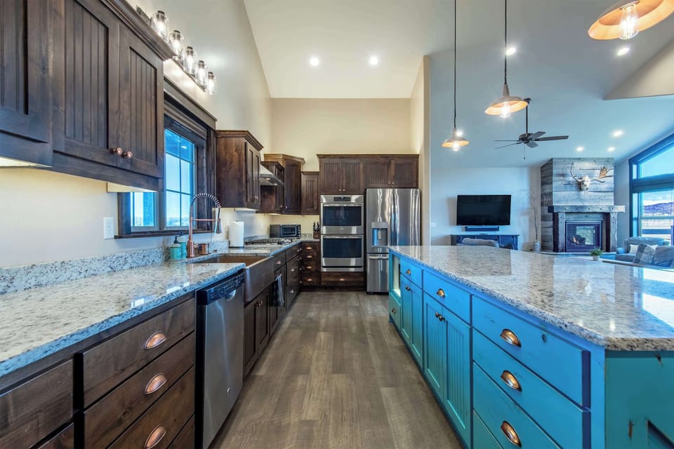 Gourmet kitchen with teal island, dark cabinetry, granite counters, and full stainless suite — plenty of room to cook for 14 hungry adventurers.