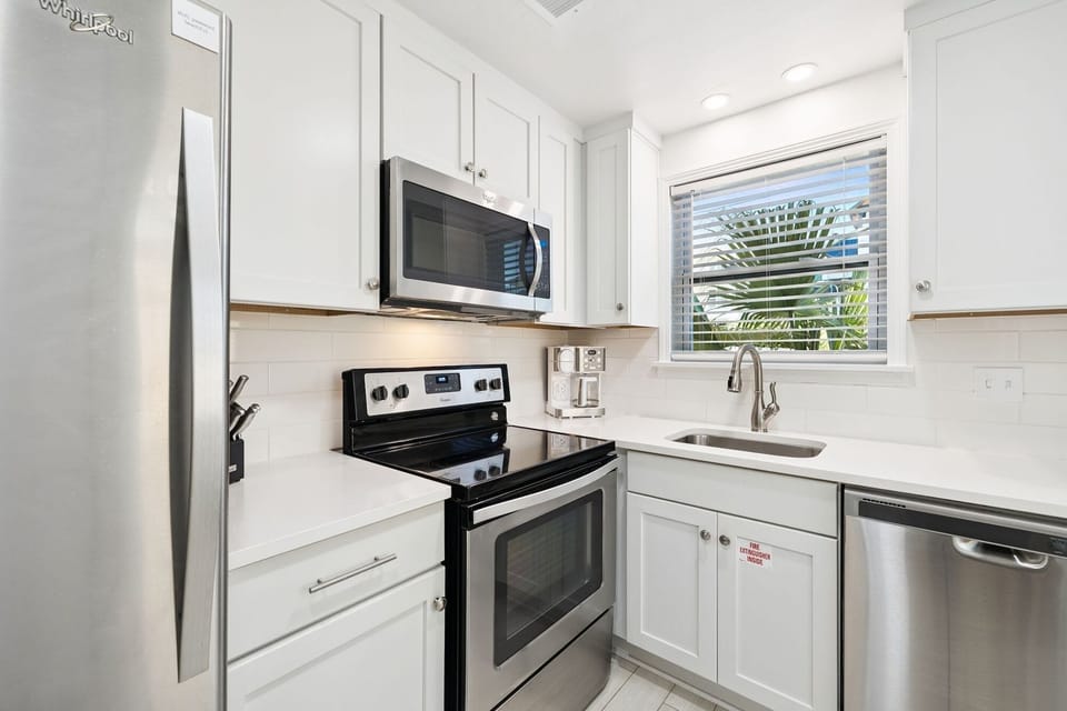 Your fully-equipped kitchen awaits with modern appliances and bright white cabinetry, perfect for preparing meals with tropical views.