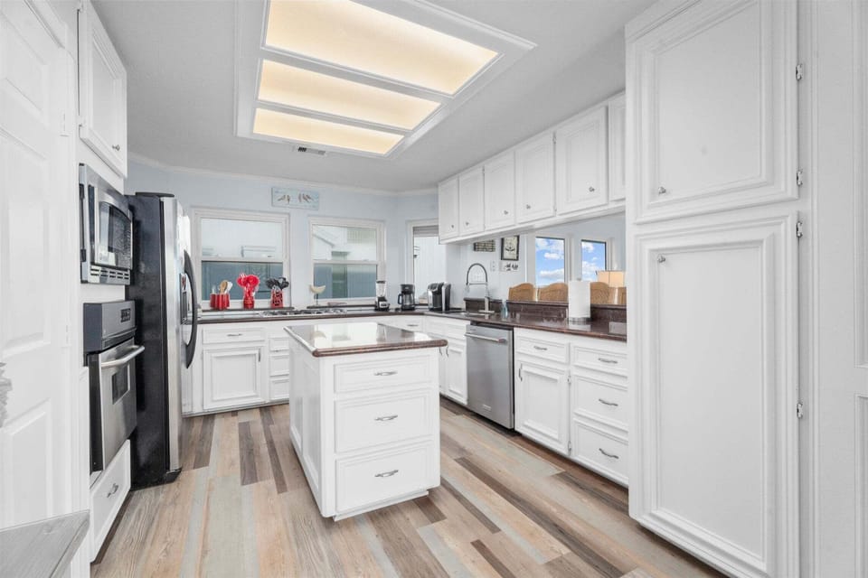 Modern white kitchen with stainless steel appliances, large center island, custom cabinetry, and bright skylight lighting in this beachfront Galveston home.