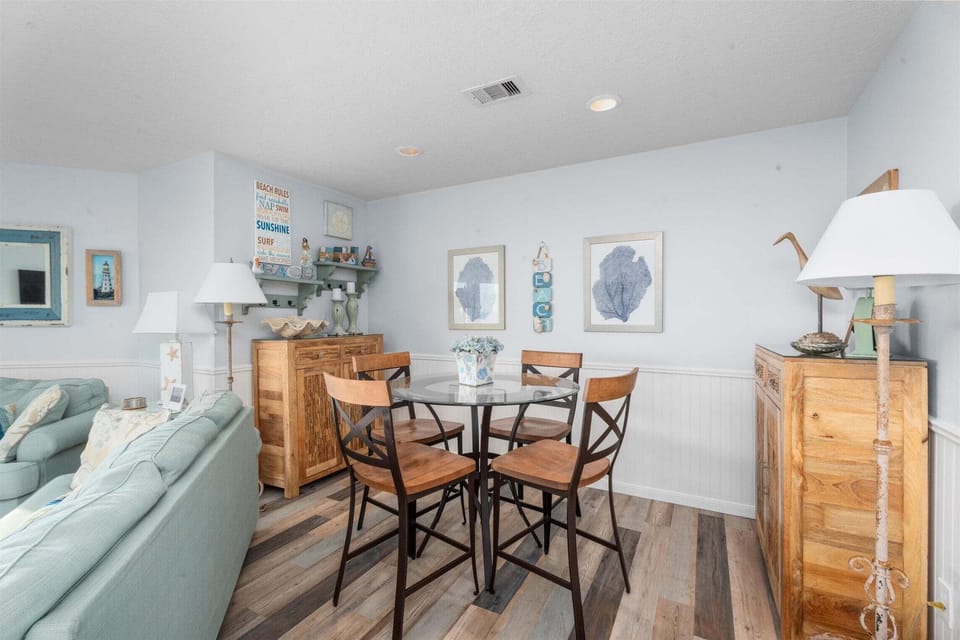 Cozy sitting area with café table, coastal artwork, and natural light. Great spot for morning coffee or relaxing indoors during your beach vacation.