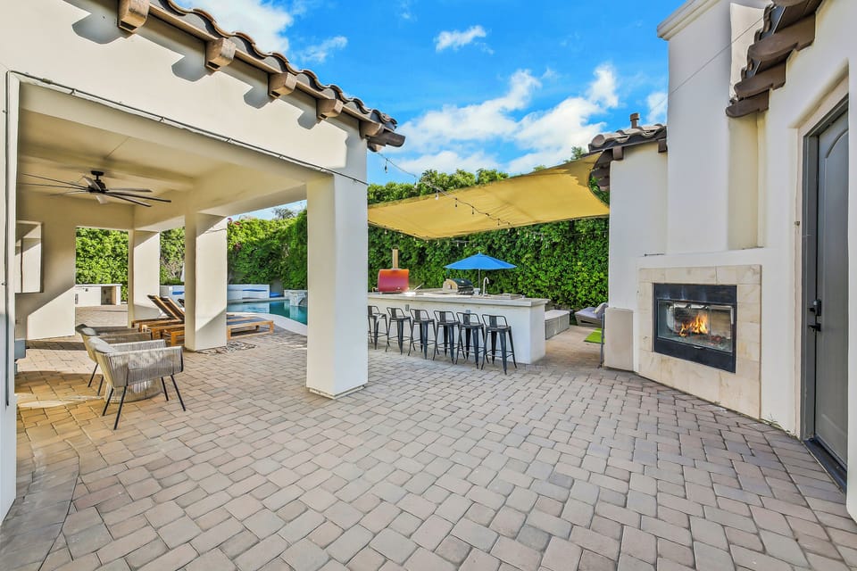 Spacious outdoor patio with a pool, outdoor kitchen, bar seating, and cozy fireplace—perfect for entertaining.