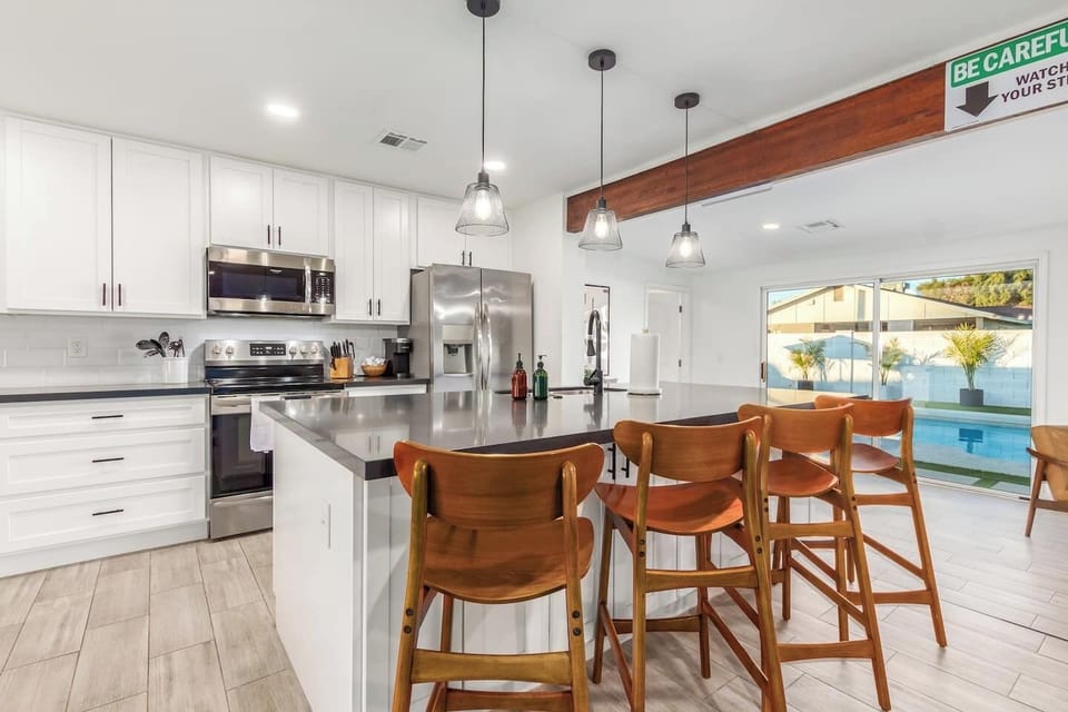 Bright, modern kitchen with white cabinetry, stainless steel appliances, a spacious island with bar seating, and sliding glass doors overlooking the pool.
