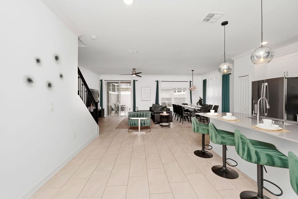 Open-concept living and dining area with modern green velvet bar stools and natural light.