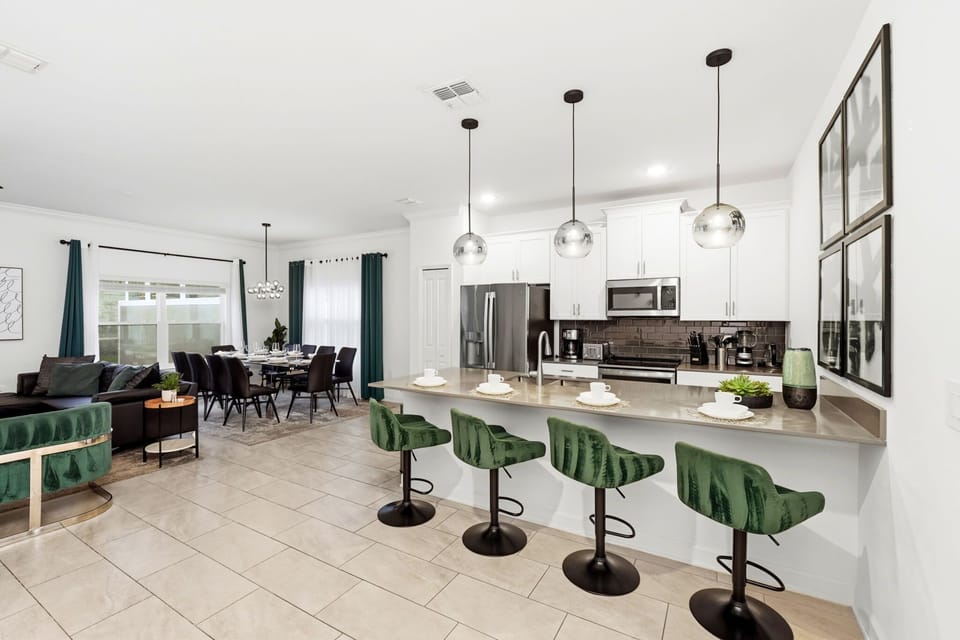 Modern kitchen with a breakfast bar featuring green velvet stools and stainless steel appliances
