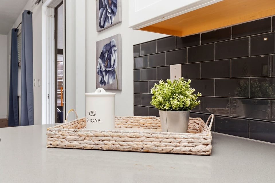A modern kitchen countertop with a decorative sugar container and potted plant on a woven tray.