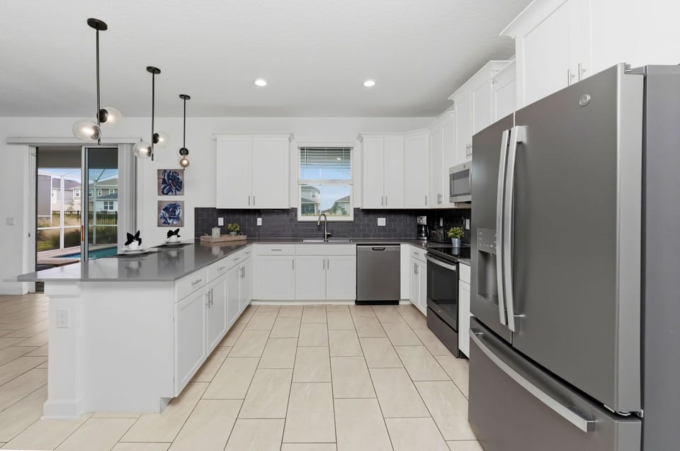 Modern kitchen with white cabinetry and stainless steel appliances overlooking the pool area.