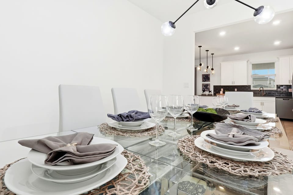 Modern dining area with glass table set for a meal and view into the kitchen