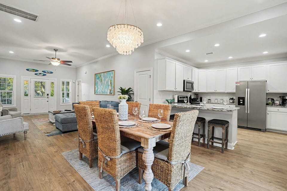 Welcome to Sea Princess: elegant dining space with woven chairs, chandelier glow, and open flow to the coastal kitchen.