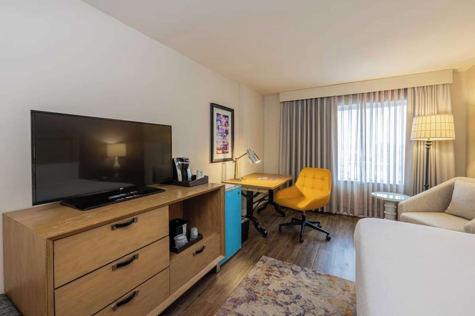 Big TV, coffee maker, work desk, and sunny window with curtains