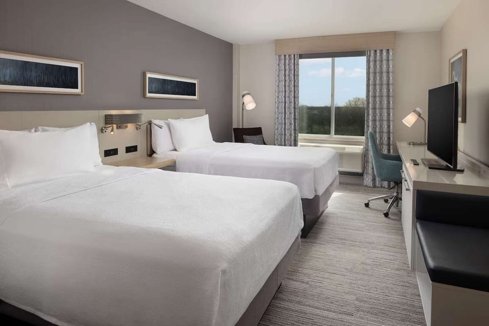 Guest room featuring two double beds, TV, work desk, and natural light