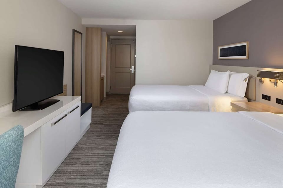 Bright guest room with two queen beds, flat-screen TV, and workspace
