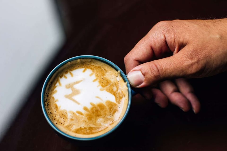Latte art in a blue cup held gently by a hand