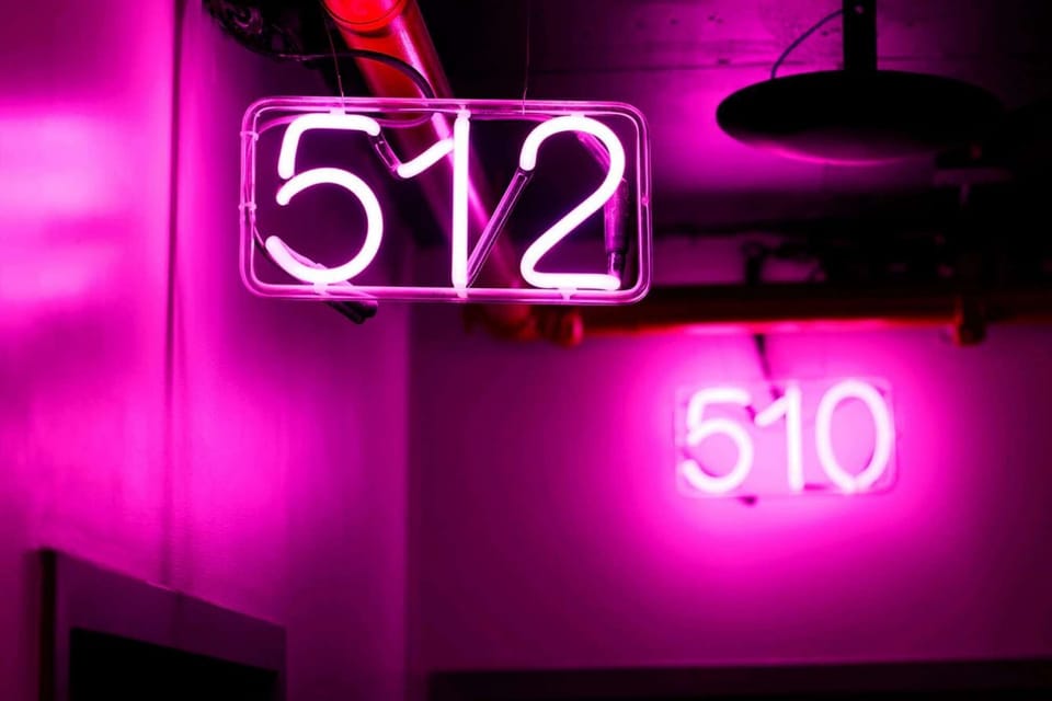 Neon room numbers glowing in vivid magenta above the hallway