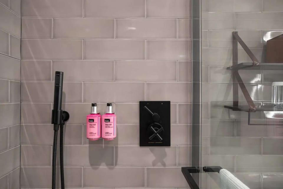 Shower with gray tiles, black fixtures, and pink toiletries