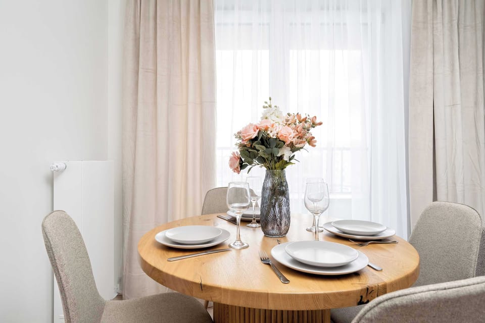 A dining table set for a meal, decorated with flowers and neatly arranged tableware in a sunlit room.