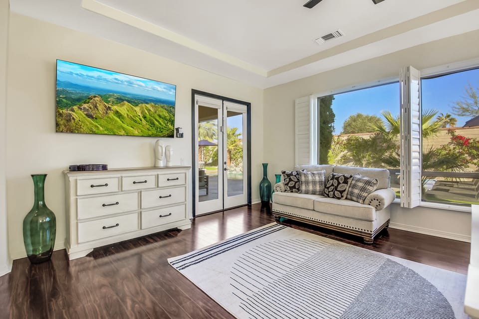Spacious bedroom with a cozy sitting area, large windows, TV, and plenty of natural light.