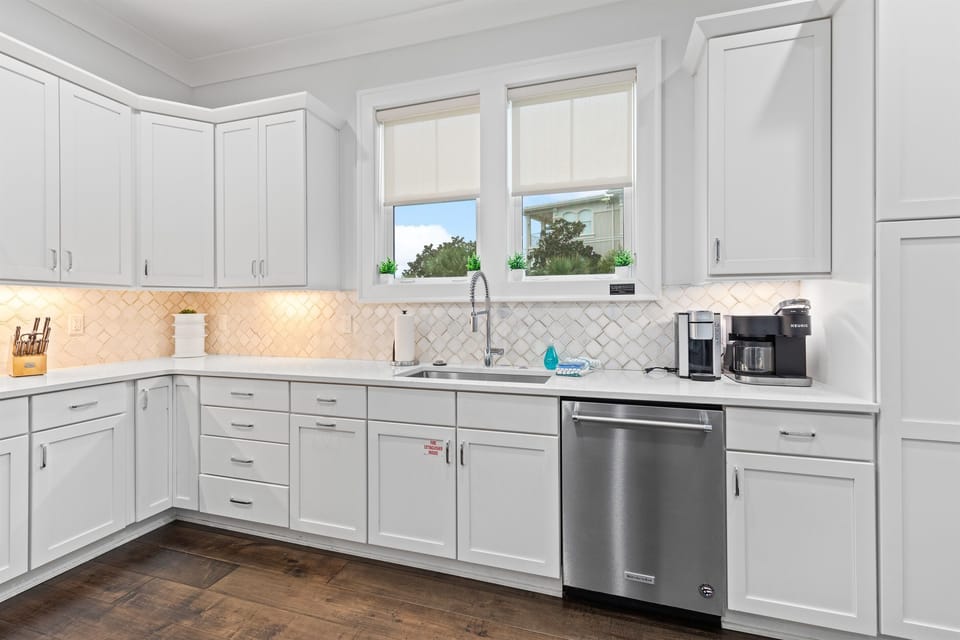 The open, fully stocked kitchen is designed for gathering, featuring abundant natural light, generous counter space, and a large island perfect for serving meals and snacks to big groups. An easy, inviting space where cooking, conversation, and connection 