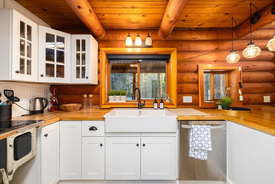 Charming meets refined. This log cabin kitchen features white cabinets, warm butcher block counters, and a beautiful white farmhouse sink. Take in the quiet forest view through the window while you prepare your meals.