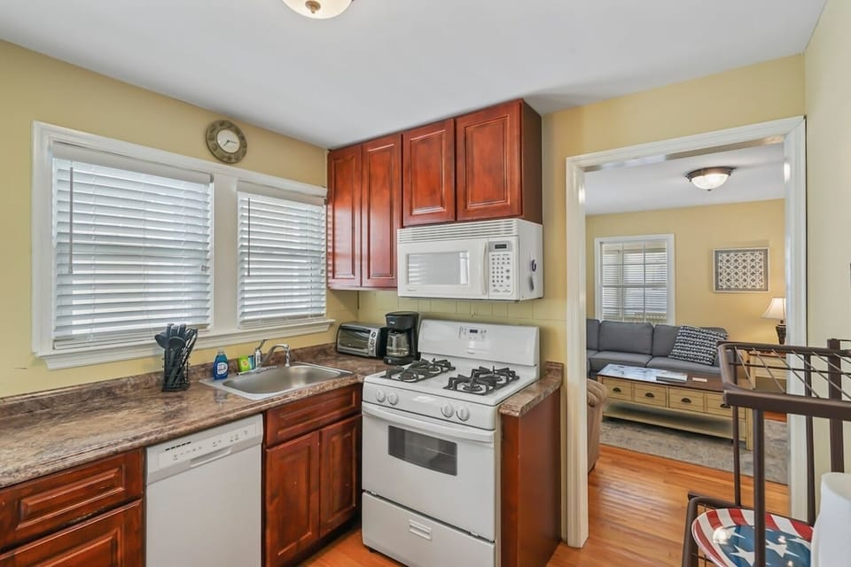 Whip up a fantastic feast in our fully equipped kitchen, featuring a modern gas stove, built-in microwave, dishwasher, and a cozy dining space. The bright, yellow walls and cherry-wood cabinets create a warm and inviting atmosphere