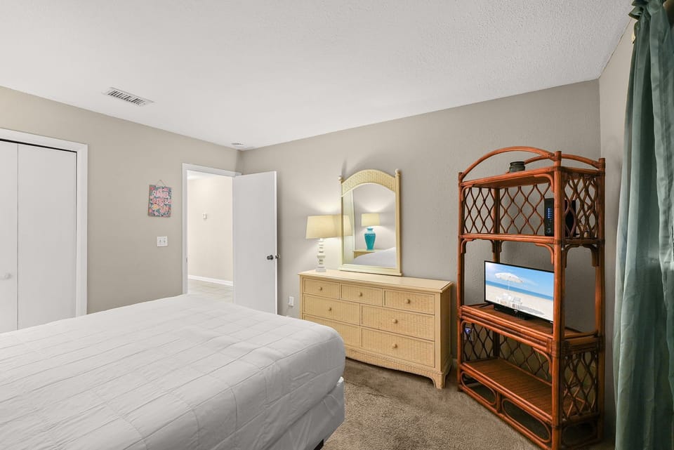Cozy bedroom featuring a dresser with mirror and a wicker shelf with television.