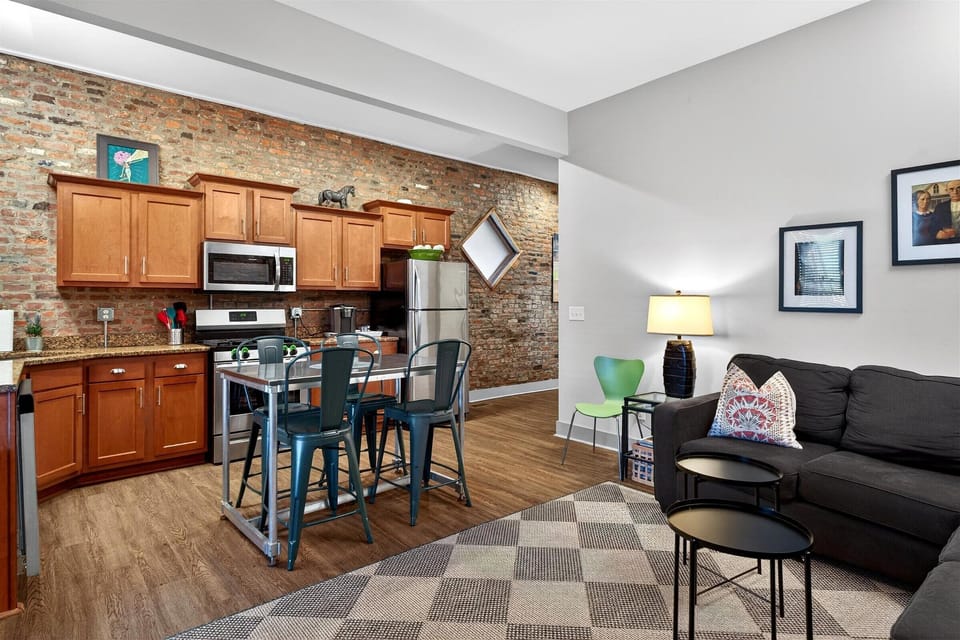 This open concept space features a comfy black sofa with colorful pillows right next to the kitchen island. It is the perfect setup for chatting with the cook while enjoying a drink.