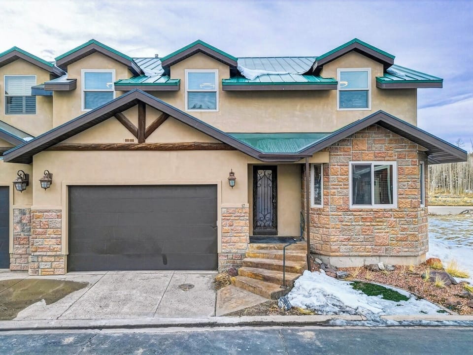 Modern townhouse exterior featuring stone accents, metal roofing, and attached garage in a scenic mountain community setting.
