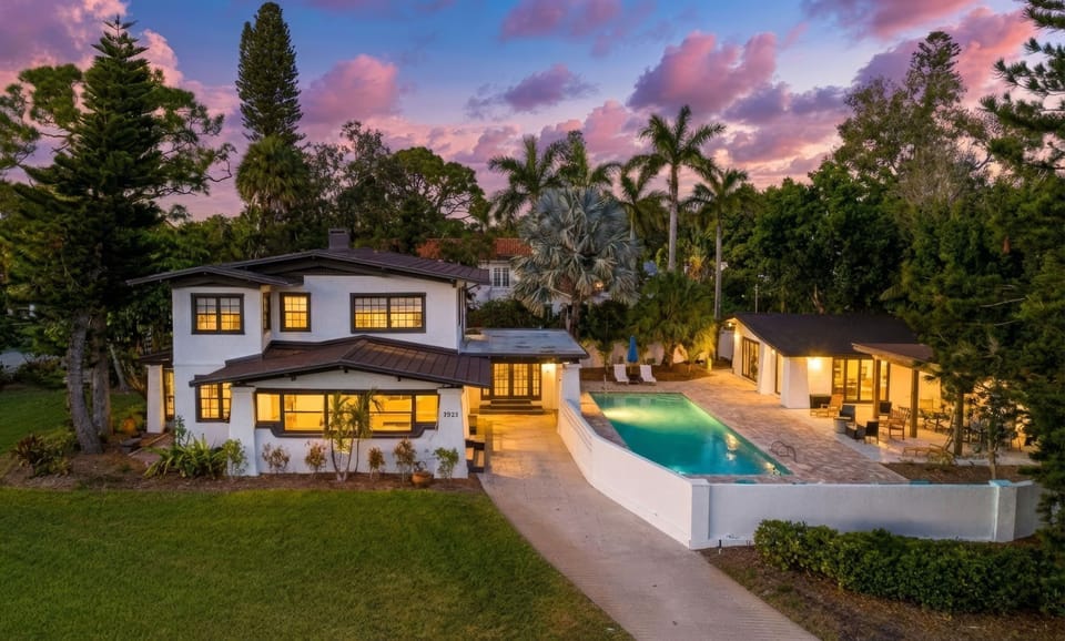 Stunning property featuring elegant architecture, sparkling pool, and lush tropical gardens beneath a breathtaking sunset sky.