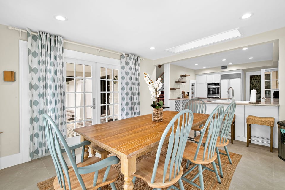 Gather around your beautiful wooden dining table with coastal-inspired chairs, perfectly positioned between the bright kitchen and patio doors.