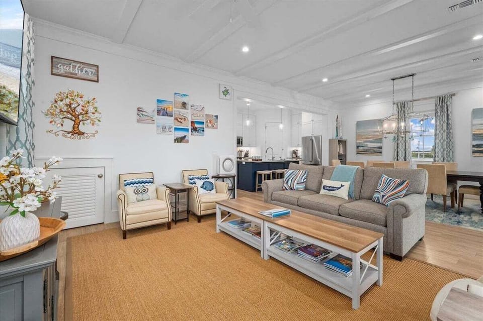 Open-concept great room combining living, dining, and kitchen areas with modern coastal design and abundant natural light.